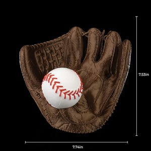 May include: A brown leather baseball glove with a white baseball inside. The baseball has red stitching. The glove is 7.74 inches wide and 7.53 inches tall. The background is black.