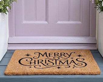 Może przedstawiać: Prostokątna wycieraczka z włókna kokosowego w kolorze brązowym z czarnym napisem Merry Christmas wykonanym ozdobną czcionką z motywem gwiazdek. Wycieraczka leży przed jasnofioletowymi drzwiami, pomiędzy dwiema białymi donicami z białymi i fioletowymi kwiatami.