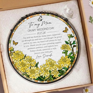 May include: A round, decorative glass piece with a black metal frame, featuring yellow floral and butterfly designs. The text reads "To my Mom, On my Wedding Day, 11.25.26" and a heartfelt message. It is presented in a gift box.