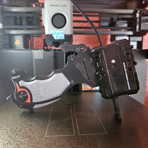 May include: A black and gray Beyblade X Winder Launcher with a textured grip and orange accents. The launcher has the text "BEYBLADE X WINDER LAUNCHER" printed on the side. The launcher is on a dark surface.