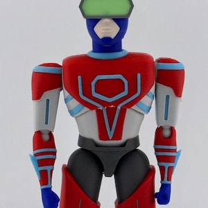 May include: A plastic action figure featuring a blue helmet with a green visor, a red and white chest plate with blue trim, and grey and red limbs. The figure has a stylized humanoid form with articulated joints and a smooth, matte finish.