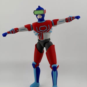 May include: A posable action figure featuring a blue, red, and white color scheme. The figure wears a blue helmet with a green visor, a red and white chest plate with a geometric design, and matching red and blue limb armor with blue fists.
