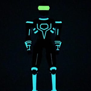 May include: A full-body suit featuring glowing cyan light strips arranged in geometric patterns across the chest, shoulders, arms, and legs, paired with a bright lime green visor, all set against a completely black background.