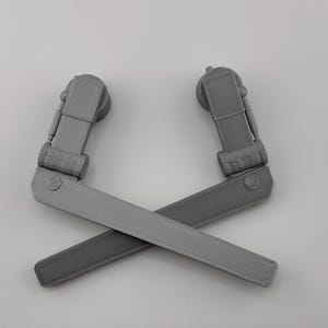 May include: Two gray plastic pieces with a hinge and a flat surface. The pieces are crossed over each other.