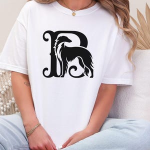 Pu&ograve; includere: T-shirt bianco con grafica nera. Il design presenta la silhouette di un cane integrata in una lettera "R" stilizzata. Il cane ha pelo lungo e corporatura snella. La maglietta &egrave; a girocollo.