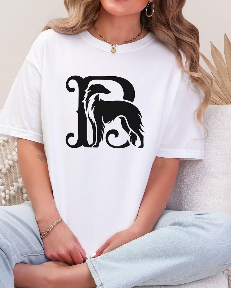 Pu&ograve; includere: T-shirt bianco con grafica nera. Il design presenta la silhouette di un cane integrata in una lettera "R" stilizzata. Il cane ha pelo lungo e corporatura snella. La maglietta &egrave; a girocollo.