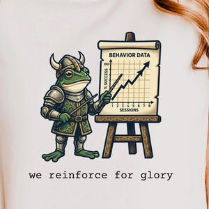May include: A white t-shirt featuring a green frog dressed in Viking armor, holding a pointer toward a chart on an easel labeled BEHAVIOR DATA with a line graph showing % SUCCESS over SESSIONS. The text below reads we reinforce for glory.