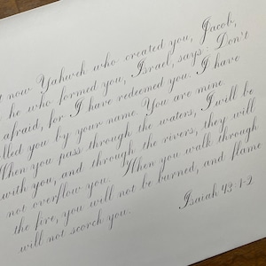 May include: A handwritten excerpt from the Bible, Isaiah 43:1-2, in elegant cursive script. The text reads: "But now Yahweh who created you, Jacob, and he who formed you, Israel, says: Don't be afraid, for I have redeemed you. I have called you by your name. You are mine. When you pass through the waters, I will be with you, and through the rivers, they will not overflow you. When you walk through the fire, you will not be burned, and flame will not scorch you."