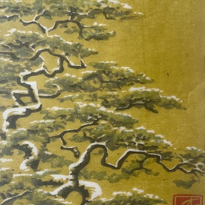 May include: An artistic print of a snow-covered pine tree with a gold background. The tree's branches are dark green and white, with a red square symbol in the lower right corner. The artwork has a traditional Japanese aesthetic.
