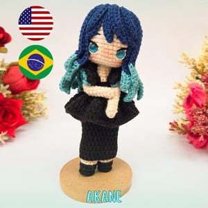 以下が含まれることがあります： 「推しの子」のキャラクター、アカネの手作りかぎ針編み人形。人形は青い髪、黒いドレス、クリーム色のトップスを着ています。上部には「PDF PATTERN / PADRÃO DIGITAL」という文字があり、下部には「AKANE (OSHI NO KO)」という名前があります。