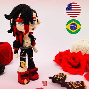 以下が含まれることがあります： 黒い髪と赤いアクセントのキャラクターの手作りの編み人形。黒いズボンと赤いブーツを履いています。人形の隣には、黒と金の編みアクセサリーのペアがあります。「PDF PATTERN / PADRÃO DIGITAL」というテキストが上部にあります。