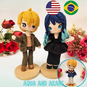 以下が含まれることがあります： 黄色い髪と茶色のジャケットのドールと、青い髪と黒いドレスの2体の編みぐるみ。木製の台座に立っています。画像には「PDF PATTERN / PADRÃO DIGITAL」と「AQUA AND AKANE」の文字が含まれています。
