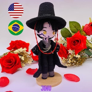 Può includere: Bambola all'uncinetto fatta a mano con cappello e abito neri, su una base di legno. La bambola ha un viso dettagliato con occhi dorati ed è circondata da rose rosse. Il testo "PDF PATTERN / PADRÃO DIGITAL" è visibile.
