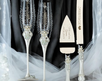 May include: Elegant wedding champagne flutes and cake serving set. The flutes are adorned with rhinestones and pearls, with the letter "W" and a heart. The cake server and knife are engraved with "Forever" and the couple's names and wedding date.