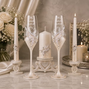 May include: Two champagne flutes and three pillar candles decorated with white pearls and clear crystals. The flutes are engraved with Mr. Eustache and Mrs. Eustache and the date 03.06.26. The candles and flutes feature matching ornate white embellishments.