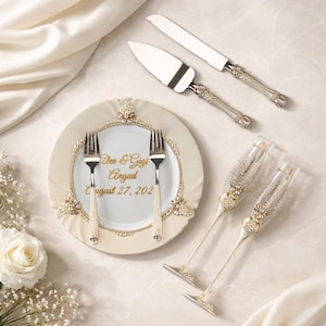 May include: Elegant wedding cake knife and server set with decorative handles, a decorative plate with two forks, and two champagne flutes. The plate has the names "Alex & Gigi Argud" and the date "August 27, 202" in gold lettering.