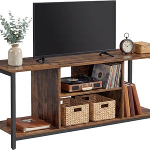 May include: A rustic-style TV stand with a dark brown wood finish and black metal frame. It features open shelving for media components, storage baskets, and a record player. A TV sits on top, with a clock and vase.