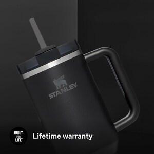 K&ouml;nnte beinhalten: Schwarzer Stanley-Becher mit Griff, Strohhalm und Deckel. Der Becher hat das Stanley-Logo und den Text "Lebenslange Garantie". Der Becher ist auf Langlebigkeit ausgelegt und ist f&uuml;r das Leben gebaut.
