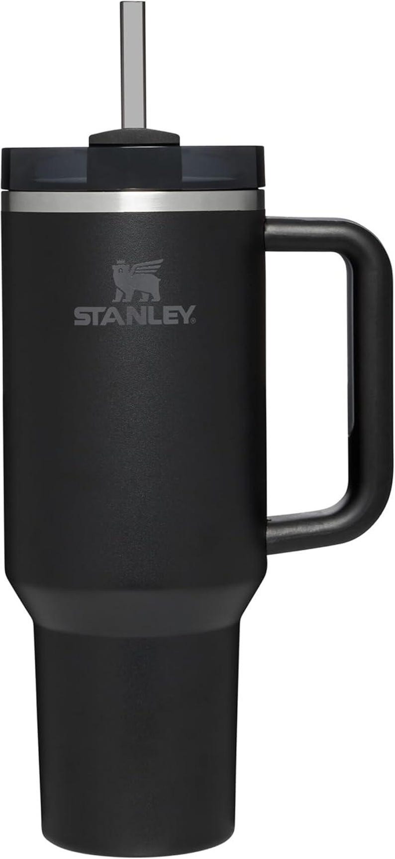 K&ouml;nnte beinhalten: Schwarzer Stanley Quencher H2.0 FlowState Becher mit Griff und wiederverwendbarem Strohhalm. Der Becher hat das Stanley-Logo auf der Vorderseite. Er ist so konzipiert, dass Getr&auml;nke stundenlang kalt bleiben.