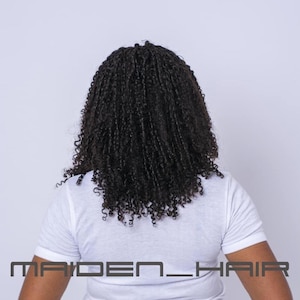 May include: A person wearing a white t-shirt with the text "MAIDEN_HAIR" at the bottom. The person has long, dark, curly hair. The background is a plain white.