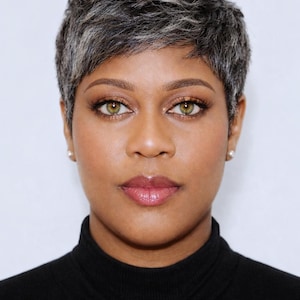 Könnte beinhalten: Porträt einer Person mit kurzen, grauen Haaren und grünen Augen. Sie trägt einen schwarzen Rollkragenpullover. Die Person hat einen neutralen Ausdruck, mit einer hellrosa Lippenfarbe und dezentem Make-up.