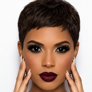 Puede incluir: Retrato en primer plano de una persona con cabello corto y castaño oscuro y maquillaje dramático. La persona tiene labios llenos y borgoña oscuro y uñas largas y blancas. Las manos de la persona están cerca de su rostro.