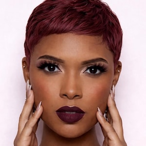 May include: A close-up portrait of a person with dark skin, wearing burgundy lipstick and matching short, textured hair. The person has long eyelashes and is touching their face with long, pointed nails.