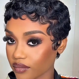 Puede incluir: Una persona con piel oscura y cabello negro corto y ondulado. Tiene labios carnosos, maquillaje de ojos oscuro y pestañas largas. Su piel tiene un brillo resaltado. Lleva una parte superior con estampado en blanco y negro.