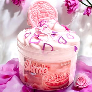 May include: A pink slime container with a pink cookie on top and heart-shaped confetti. The container has the text "my Valen Slime" and "Do not eat". The slime is decorated with pink hearts and a pink cookie.