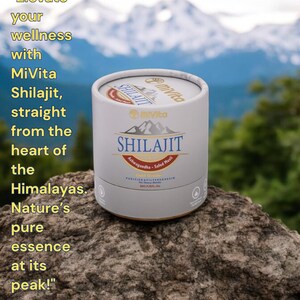 May include: A white cylindrical container with a gold lid and label. The label reads "MiVita Shilajit Ashwagandha - Safed Musli" and features a mountain range graphic. The container is sitting on a rock with a snowy mountain range in the background.