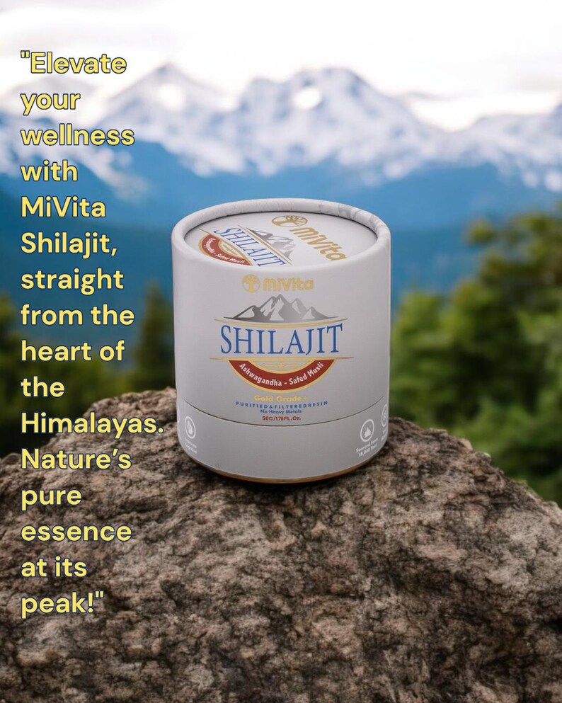 May include: A white cylindrical container with a gold lid and label. The label reads "MiVita Shilajit Ashwagandha - Safed Musli" and features a mountain range graphic. The container is sitting on a rock with a snowy mountain range in the background.