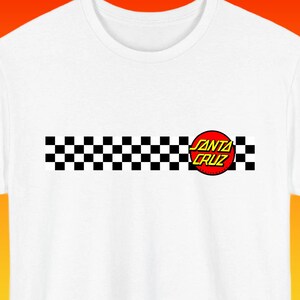 Puede incluir: Una camiseta blanca con una franja horizontal de cuadros negros y blancos en el pecho. En el lado derecho de la franja, hay un logotipo circular rojo con borde amarillo que contiene el texto SANTA CRUZ en letras amarillas en negrita.