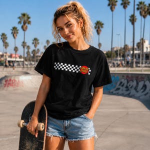 Puede incluir: Una camiseta negra de manga corta con un patr&oacute;n de cuadros blanco y negro horizontal en el pecho, acentuado por un logotipo circular rojo con el texto Santa Cruz impreso en letras amarillas en el lado derecho del gr&aacute;fico.