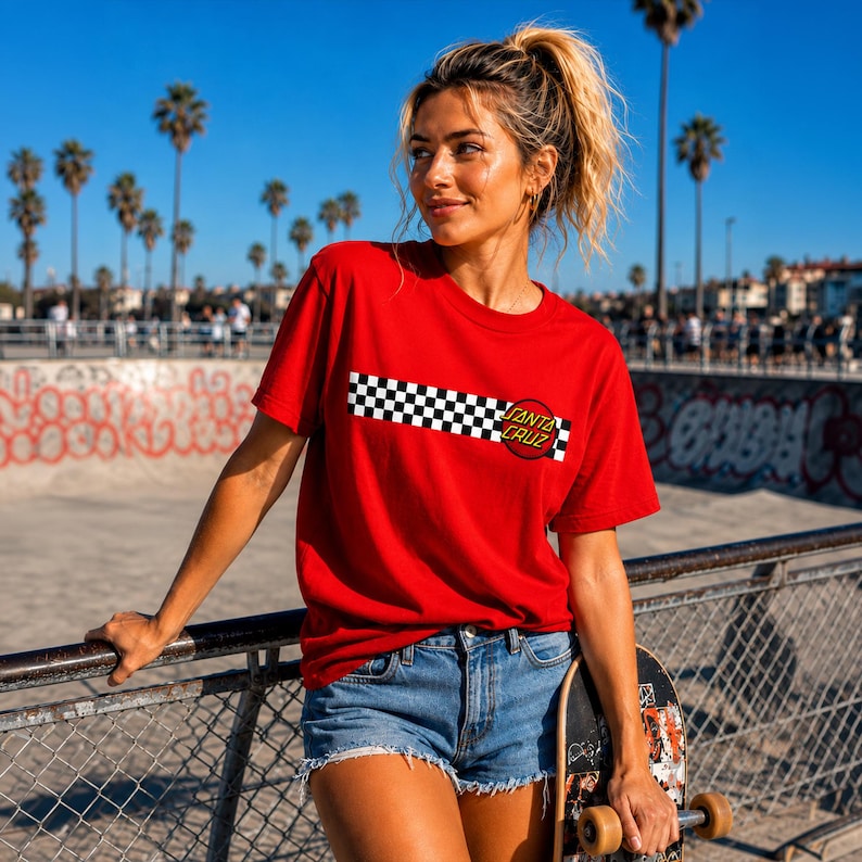 Puede incluir: Una camiseta roja de manga corta con una franja horizontal de cuadros blancos y negros en el pecho. Un logotipo circular rojo con el texto Santa Cruz est&aacute; situado en el lado derecho de la franja de cuadros en la parte frontal de la prenda.