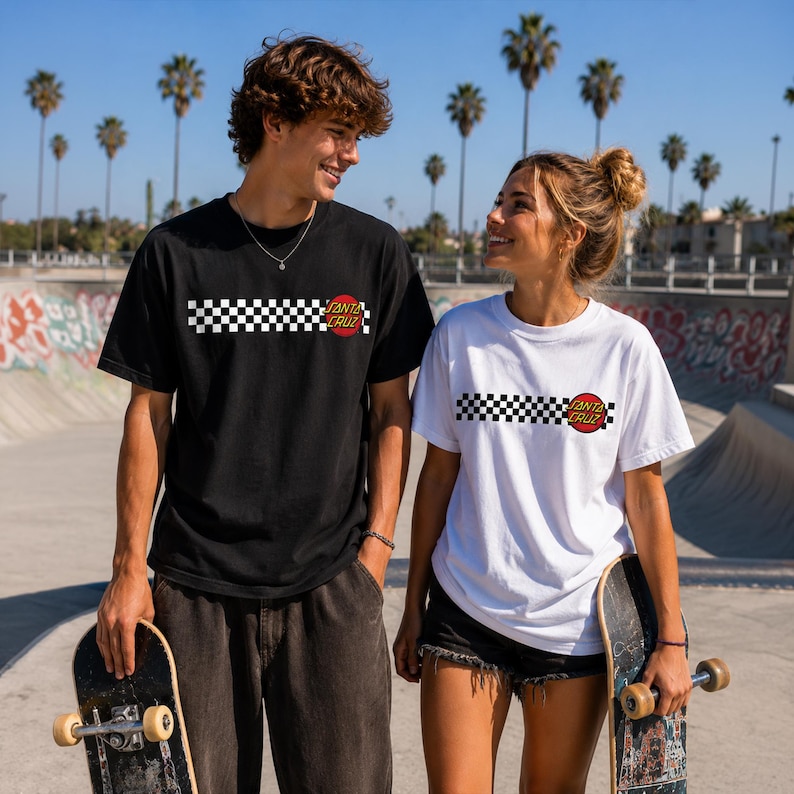Puede incluir: Una camiseta negra y una camiseta blanca, ambas con un patr&oacute;n de tablero de ajedrez horizontal en blanco y negro en el pecho y un logotipo circular rojo y amarillo de Santa Cruz en el lado derecho. Cada camiseta tiene mangas cortas y cuello redondo.