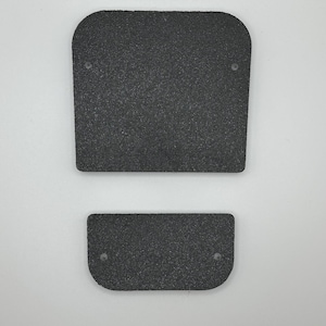 May include: Two black, textured rectangular pads with rounded corners. The larger pad has two small holes near the top, and the smaller pad has two holes near the bottom. The pads are set against a white background.