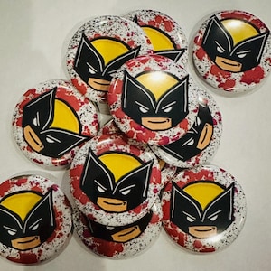 Peut inclure: Plusieurs boutons ronds avec un design Wolverine. Chaque bouton a un fond jaune avec un masque noir et des éclaboussures rouges. Les boutons sont disposés de manière légèrement superposée.