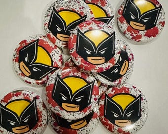 May include: A collection of round buttons featuring a Wolverine design. Each button has a yellow background with a black mask and red splatter details. The buttons are arranged in a slightly overlapping pattern.