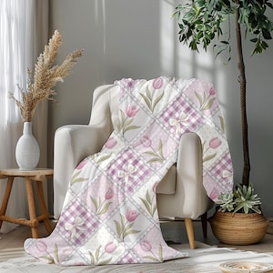 May include: A soft, quilted throw blanket draped over a chair. The blanket features a patchwork design with squares of pink tulips, gingham, polka dots, and bows. The color palette includes shades of pink, white, and green.
