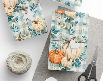 Op de afbeelding: Cadeaus verpakt met een pompoen- en bladerenpatroon op een blauw-witte geruite achtergrond. De cadeaus zijn vastgebonden met touw en versierd met witte hartvormige labels. Een bol touw, een schaar en meer labels zijn ook zichtbaar.