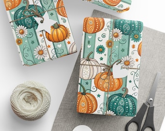 Op de afbeelding: Drie ingepakte cadeaus met pompoen- en bloempatroonpapier. Het papier heeft oranje, blauwgroene en witte pompoenen, madeliefjes en sterren op een gestreepte achtergrond. Elk cadeau is vastgebonden met touw en een wit label. Een bol touw, een schaar en blanco labels zijn ook zichtbaar.