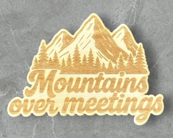 Może przedstawiać: Drewniany znak w kształcie góry z napisem "Mountains over meetings" w kursywie. Projekt obejmuje pasmo górskie i drzewa. Znak jest wykonany z jasnego drewna.
