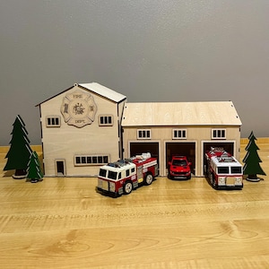 以下が含まれることがあります： 3 つのガレージドア、2 台の赤いおもちゃの消防車、赤いおもちゃの車が付いた木製の消防署のおもちゃ。消防署には「Fire Dept.」と書かれた看板があります。