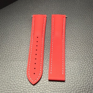 Puede incluir: Dos correas de reloj rojo brillante con costuras blancas. Una correa tiene m&uacute;ltiples agujeros para ajuste. Las correas est&aacute;n hechas de un material texturizado y est&aacute;n dise&ntilde;adas para sujetarse a un reloj.