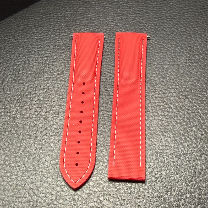 Puede incluir: Dos correas de reloj rojo brillante con costuras blancas. Una correa tiene m&uacute;ltiples agujeros para ajuste. Las correas est&aacute;n hechas de un material texturizado y est&aacute;n dise&ntilde;adas para sujetarse a un reloj.