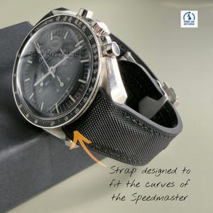 Puede incluir: Un reloj cronógrafo Omega Speedmaster plateado con esfera negra y correa texturizada negra. El reloj cuenta con un bisel taquimétrico, tres subesferas y manecillas plateadas. Una flecha naranja señala la correa con el texto, Strap designed to fit the curves of the Speedmaster.