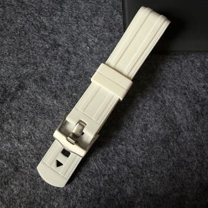 Puede incluir: Correa de reloj color crema con hebilla de acero inoxidable. La correa tiene un dise&ntilde;o acanalado y forma rectangular. La hebilla es plateada y tiene cierre de clip. La correa es de material flexible.