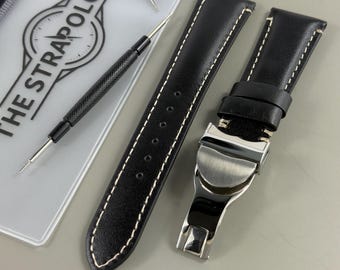 May include: Black leather watch strap with white stitching and a silver clasp. The strap is shown with a watch tool and a clear plastic sleeve with the text "THE STRAPOLOGIST".