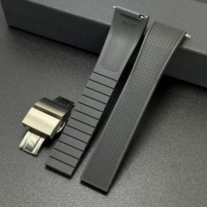 May include: Black watch straps with a silver clasp. One strap has a ribbed design, the other has a textured pattern. The text "XD-20" is visible on one of the straps. The straps are made of a flexible material.