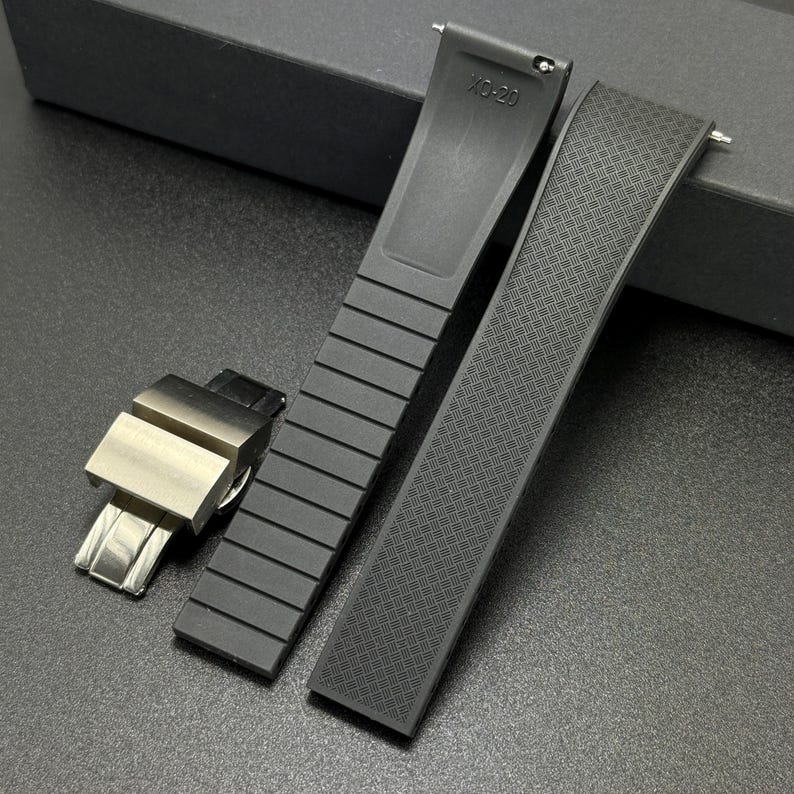 May include: Black watch straps with a silver clasp. One strap has a ribbed design, the other has a textured pattern. The text "XD-20" is visible on one of the straps. The straps are made of a flexible material.